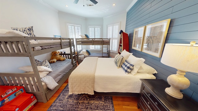 bedroom with crown molding, wooden walls, visible vents, and wood finished floors