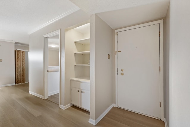 interior space featuring light wood finished floors, a textured ceiling, baseboards, and crown molding