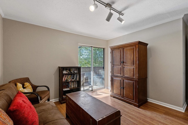 living area featuring baseboards, ornamental molding, a textured ceiling, and light wood-style floors