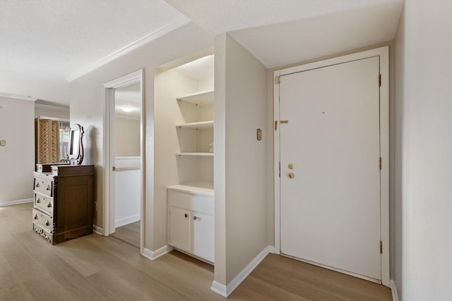 interior space featuring light wood-type flooring, baseboards, ornamental molding, and a textured ceiling