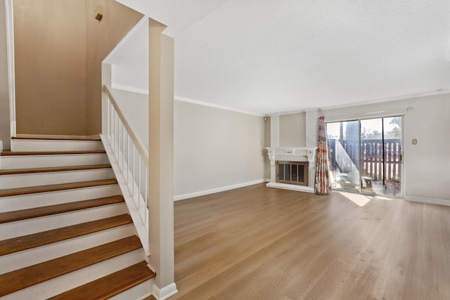 unfurnished living room featuring crown molding, a fireplace, wood finished floors, baseboards, and stairs