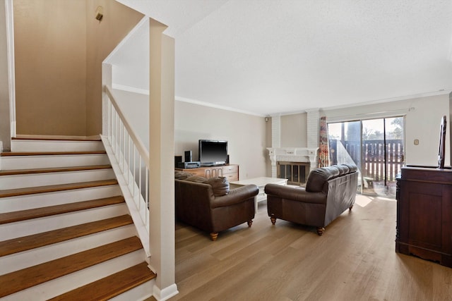 living room featuring stairway, crown molding, a textured ceiling, light wood-style floors, and a fireplace