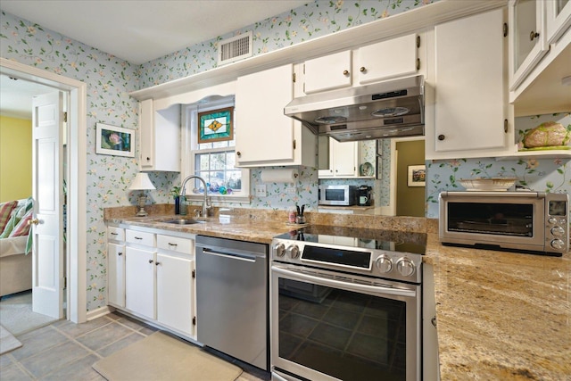 kitchen with under cabinet range hood, white cabinetry, stainless steel appliances, and wallpapered walls