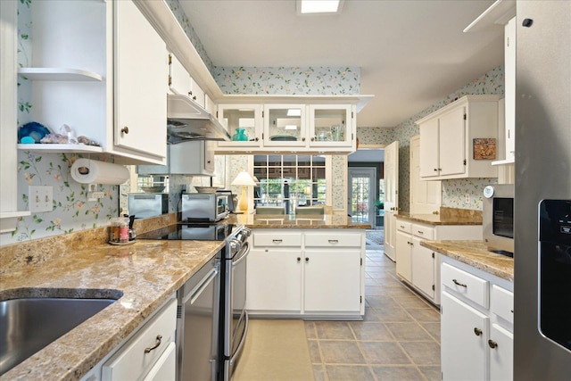 kitchen with wallpapered walls, light stone counters, stainless steel appliances, under cabinet range hood, and white cabinetry