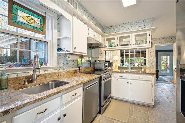 kitchen with light stone countertops, white cabinetry, a sink, and wallpapered walls