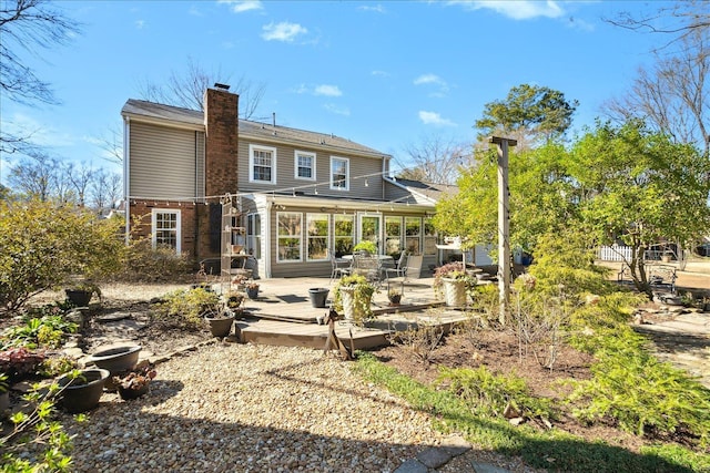 rear view of property featuring a sunroom, a chimney, brick siding, and a wooden deck