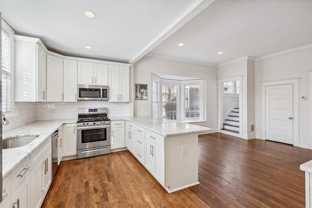 kitchen with a peninsula, white cabinets, stainless steel appliances, and dark wood finished floors