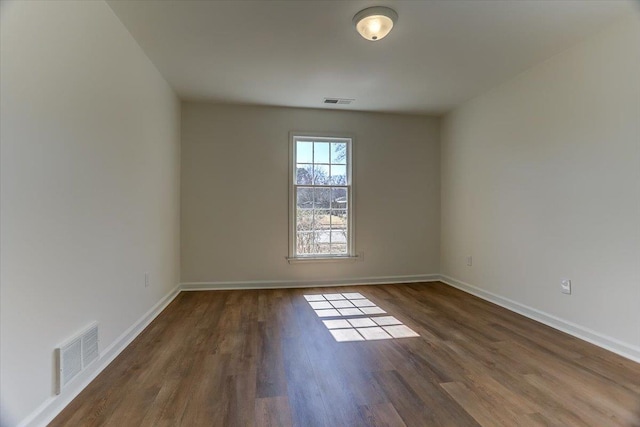 empty room featuring dark wood-style floors, visible vents, and baseboards