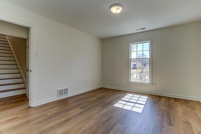 unfurnished room with stairway, wood finished floors, visible vents, and baseboards