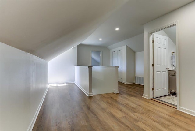 additional living space featuring light wood-style floors, lofted ceiling, visible vents, and baseboards