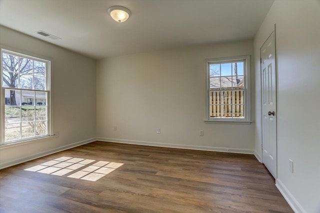 empty room with dark wood-type flooring, visible vents, and baseboards