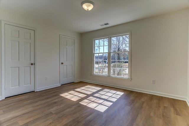 unfurnished bedroom with dark wood-style flooring, visible vents, and baseboards