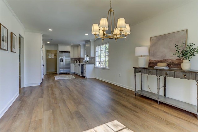 kitchen with pendant lighting, stainless steel refrigerator with ice dispenser, light wood finished floors, ornamental molding, and white cabinets