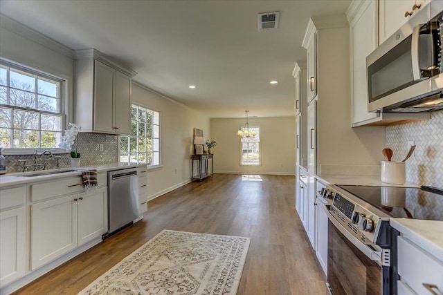 kitchen with stainless steel appliances, wood finished floors, a sink, visible vents, and white cabinets