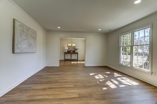 empty room featuring baseboards, ornamental molding, a chandelier, and wood finished floors