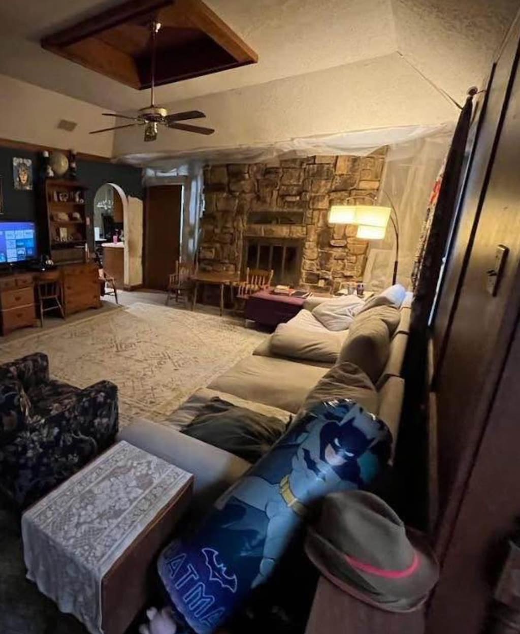 living area featuring a ceiling fan, a tray ceiling, a stone fireplace, and arched walkways