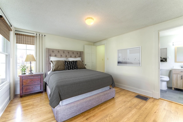 bedroom with a textured ceiling, light wood finished floors, connected bathroom, and visible vents