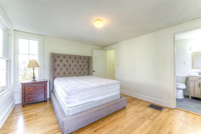 bedroom featuring light wood-style floors, baseboards, visible vents, and a textured ceiling