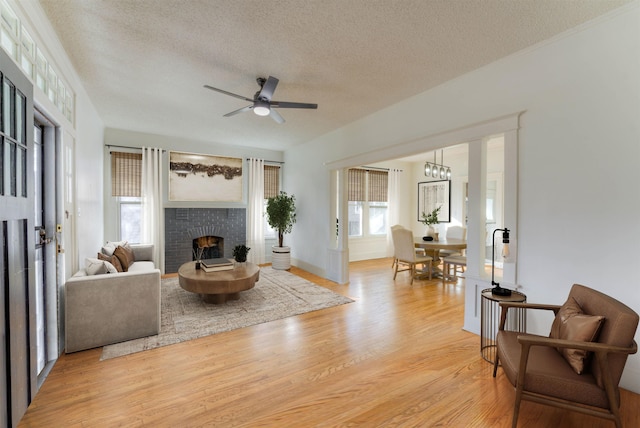 living room featuring a textured ceiling, a fireplace, light wood-style flooring, and a ceiling fan