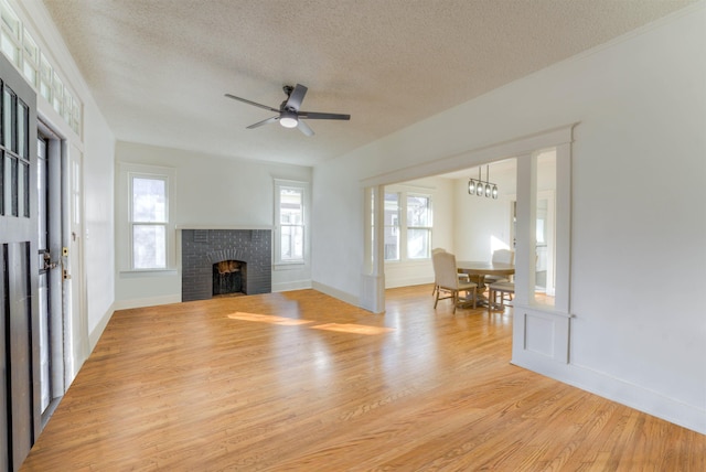 unfurnished living room with a textured ceiling, ceiling fan, a fireplace, and light wood-style flooring