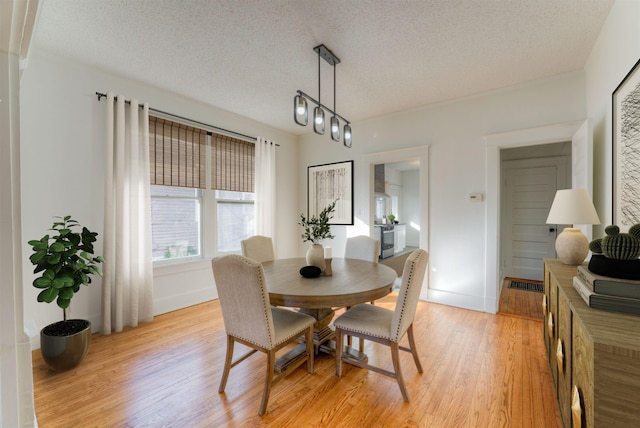 dining room with light wood-style flooring, baseboards, and a textured ceiling