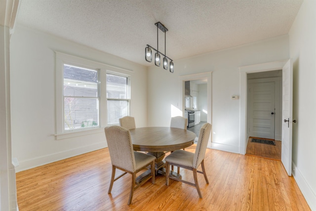 dining room featuring light wood finished floors, baseboards, and a textured ceiling