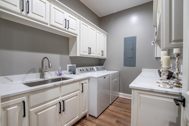 laundry area featuring light wood finished floors, cabinet space, a sink, washer and dryer, and electric panel