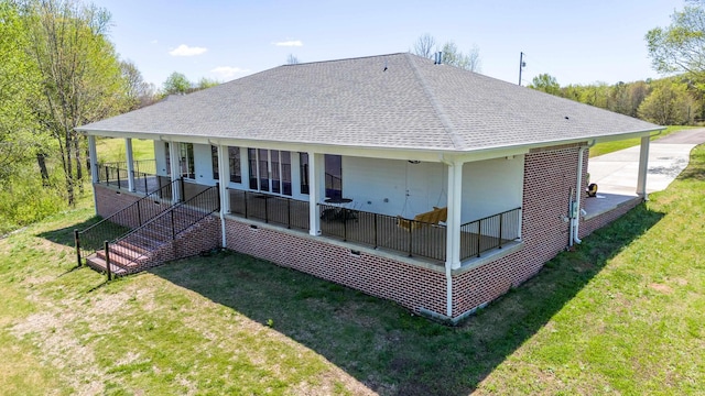 rear view of property with covered porch, a shingled roof, and a yard