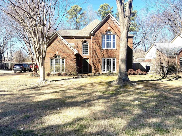 traditional-style home featuring brick siding, a front yard, and fence