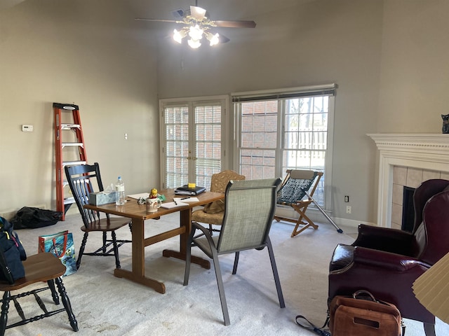 dining space featuring a tile fireplace, light colored carpet, visible vents, a ceiling fan, and a towering ceiling