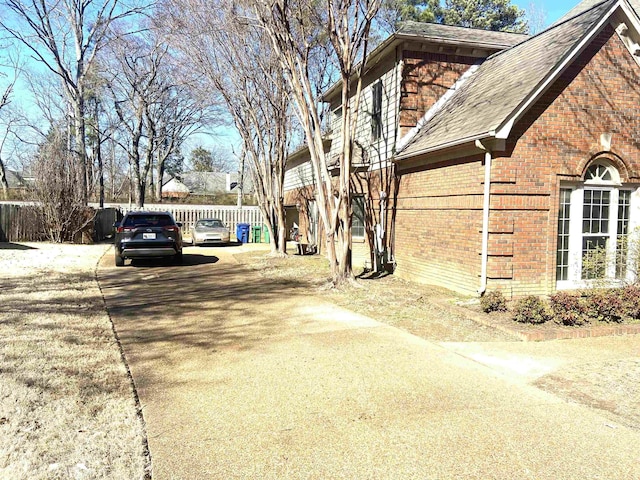 view of home's exterior with a shingled roof, fence, and brick siding