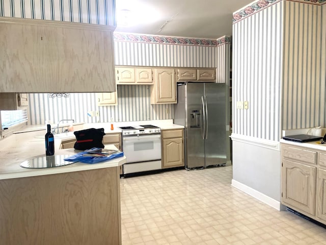 kitchen with wallpapered walls, stainless steel fridge, light countertops, white gas stove, and light floors