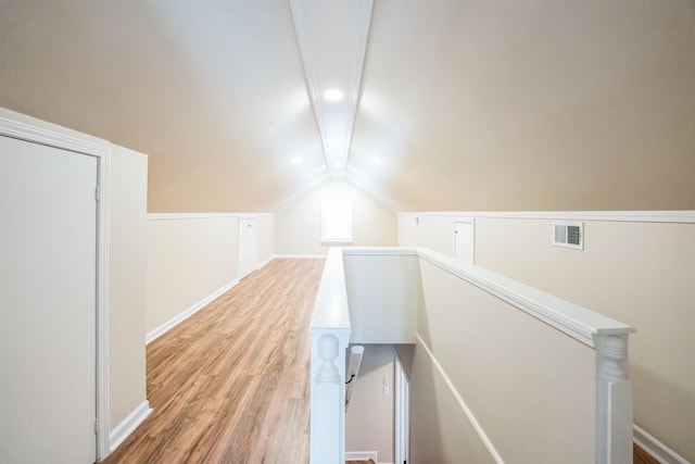 hall featuring visible vents, lofted ceiling with beams, light wood-style flooring, an upstairs landing, and baseboards