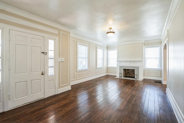 unfurnished living room featuring baseboards, a tile fireplace, ornamental molding, dark wood-type flooring, and a decorative wall