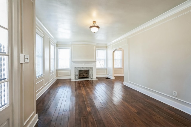 unfurnished living room featuring arched walkways, a decorative wall, a fireplace, dark wood finished floors, and crown molding