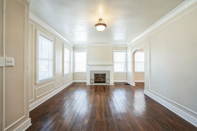 unfurnished living room featuring a wealth of natural light, dark wood-style flooring, and a decorative wall