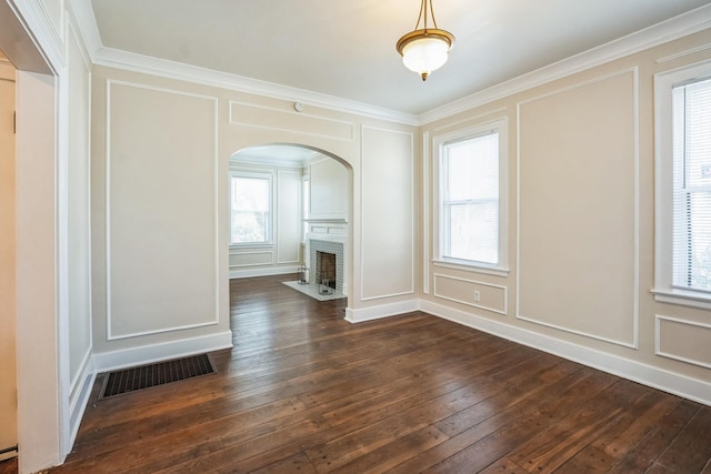 unfurnished dining area featuring arched walkways, dark wood-style floors, visible vents, and a decorative wall