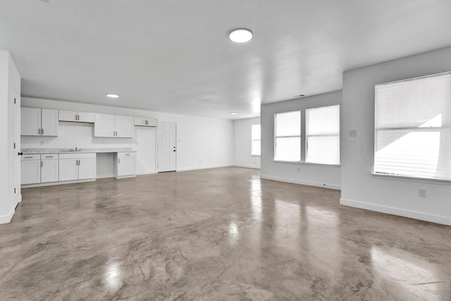 unfurnished living room with a sink, baseboards, and concrete flooring