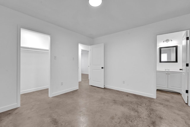 unfurnished bedroom featuring finished concrete flooring, a spacious closet, ensuite bathroom, and baseboards