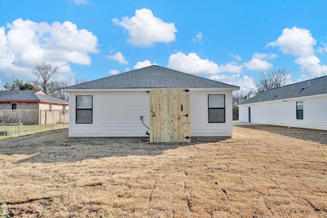 rear view of property with a yard, roof with shingles, and fence