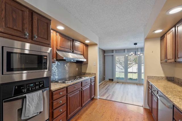 kitchen with tasteful backsplash, light wood-style floors, stainless steel appliances, a textured ceiling, and under cabinet range hood