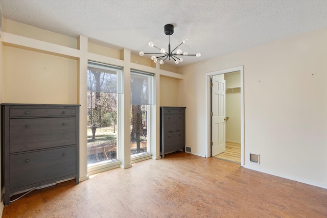 spare room featuring a chandelier, light wood-style flooring, a textured ceiling, and baseboards