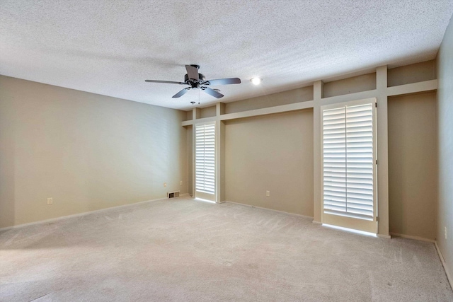 unfurnished room with visible vents, a textured ceiling, a ceiling fan, and light colored carpet