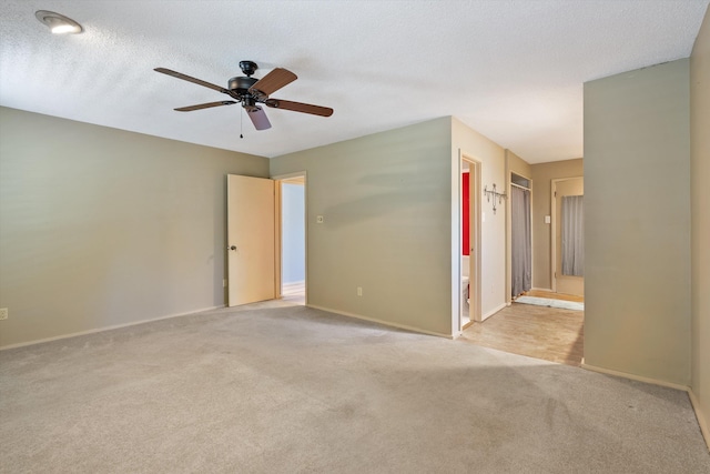 empty room featuring light carpet, ceiling fan, a textured ceiling, and baseboards