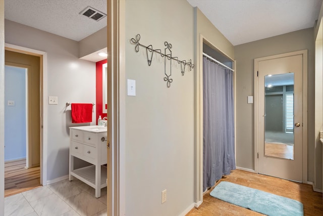 hall with a textured ceiling, visible vents, and baseboards