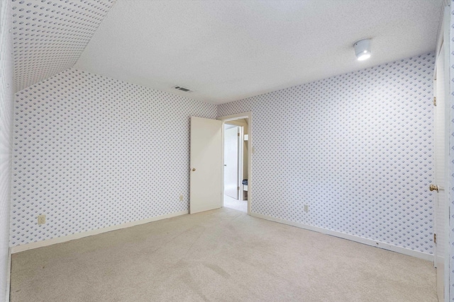 carpeted empty room featuring a textured ceiling, visible vents, and wallpapered walls