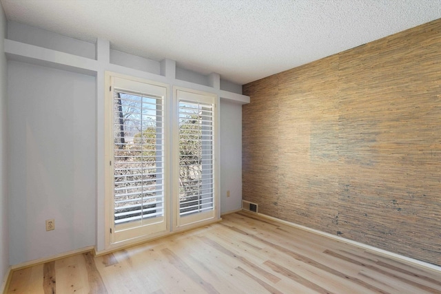 empty room with baseboards, a textured ceiling, visible vents, and wood finished floors