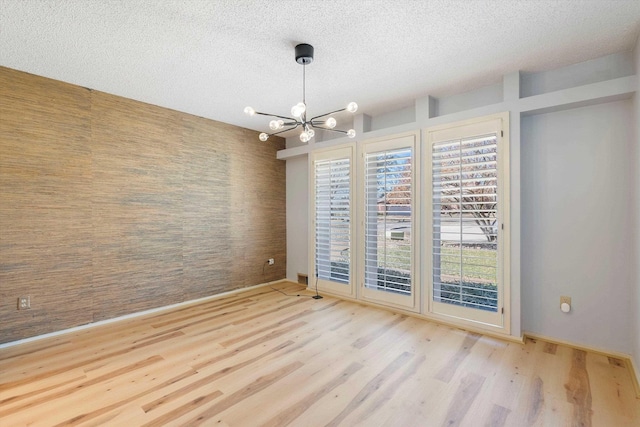 unfurnished room featuring a textured ceiling, an accent wall, wood finished floors, and a notable chandelier