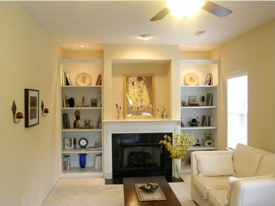 living room featuring built in shelves, a fireplace, visible vents, ceiling fan, and baseboards