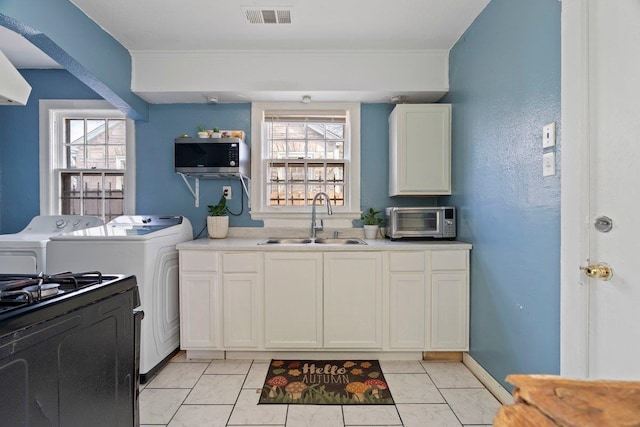 kitchen with visible vents, white cabinets, stainless steel microwave, light countertops, and a sink